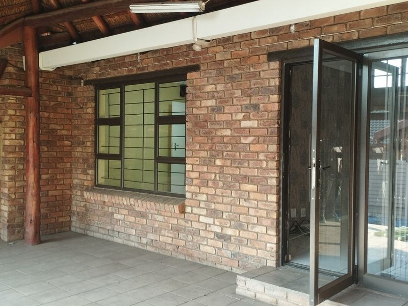 A covered patio area featuring exposed brickwork, a thatched roof, tiled flooring, and direct access to the interior through aluminium doors.