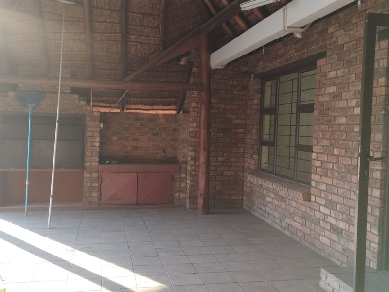 Covered outdoor patio area featuring a thatched roof, exposed timber beams, and a built-in brick braai, providing a rustic space for outdoor entertaining.