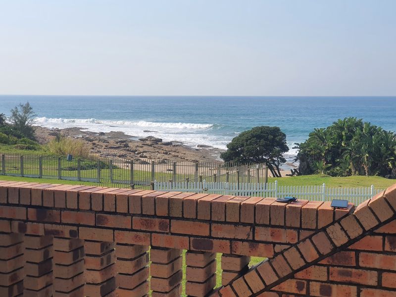 A scenic coastal view overlooking the ocean, featuring a brick balustrade in the foreground and established garden grounds with perimeter fencing.