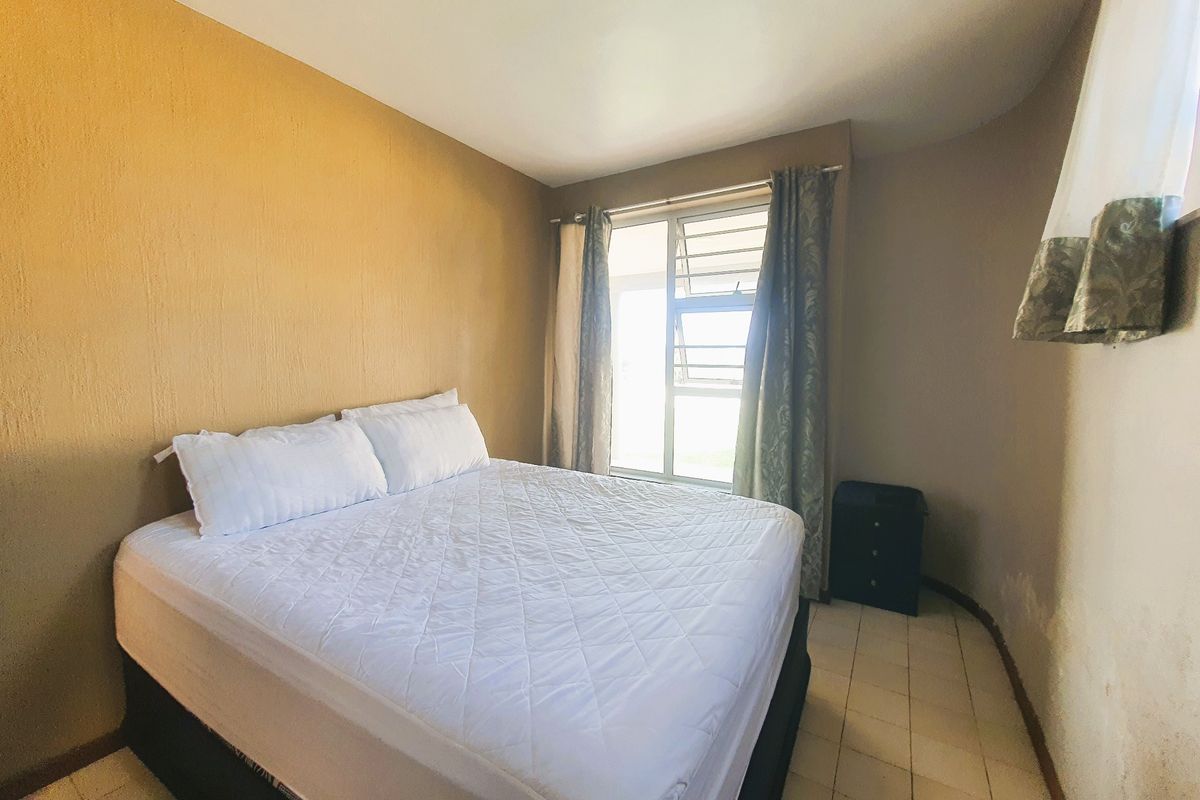 A bedroom featuring tiled flooring and a louvre window, showing signs of wear on the wall surfaces.