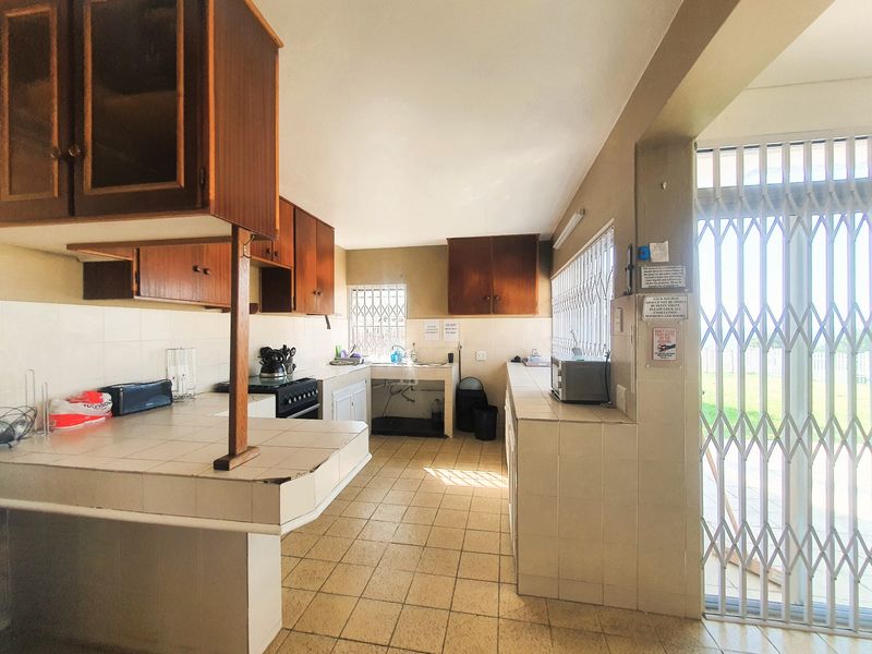 A dated kitchen featuring tiled countertops, wooden cabinetry, and tiled flooring, with direct access to an outdoor area through a security gate.