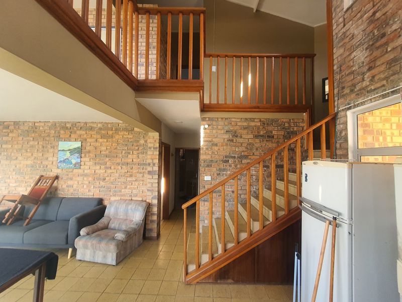 Spacious living area featuring exposed brick walls, a timber staircase with mezzanine landing, and tiled flooring throughout.