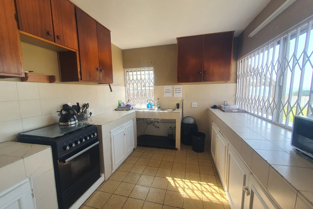 A dated kitchen featuring tiled countertops, built-in wooden cabinetry, and security bars on the windows, offering a functional layout in need of modernization.