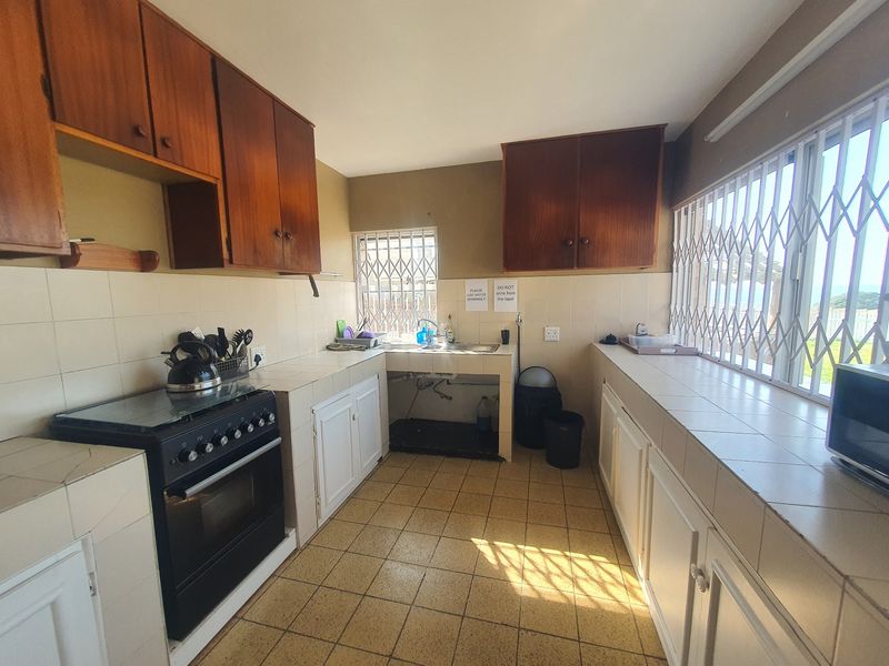 A dated kitchen featuring tiled countertops, built-in wooden cabinetry, and security bars on the windows, offering a functional layout in need of modernization.