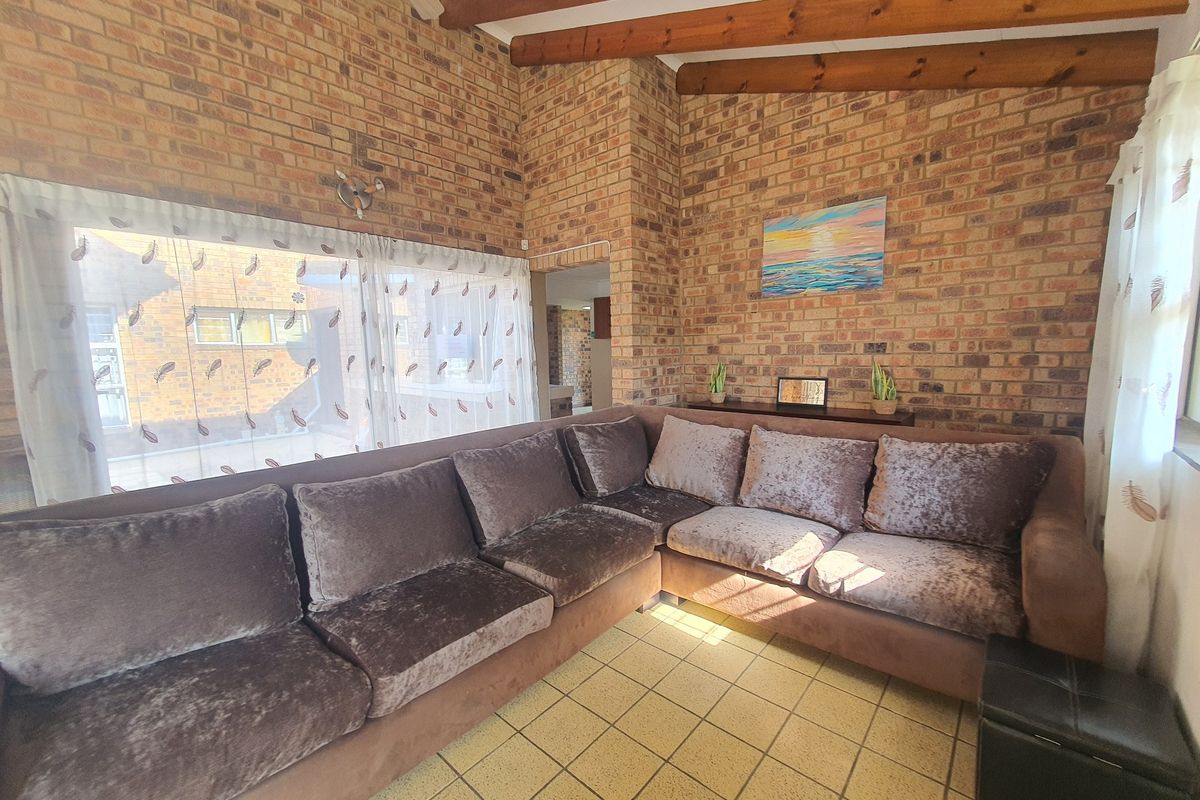 A living room featuring exposed brick walls, vaulted ceiling with timber beams, and tiled flooring, offering a rustic and character-filled living space.