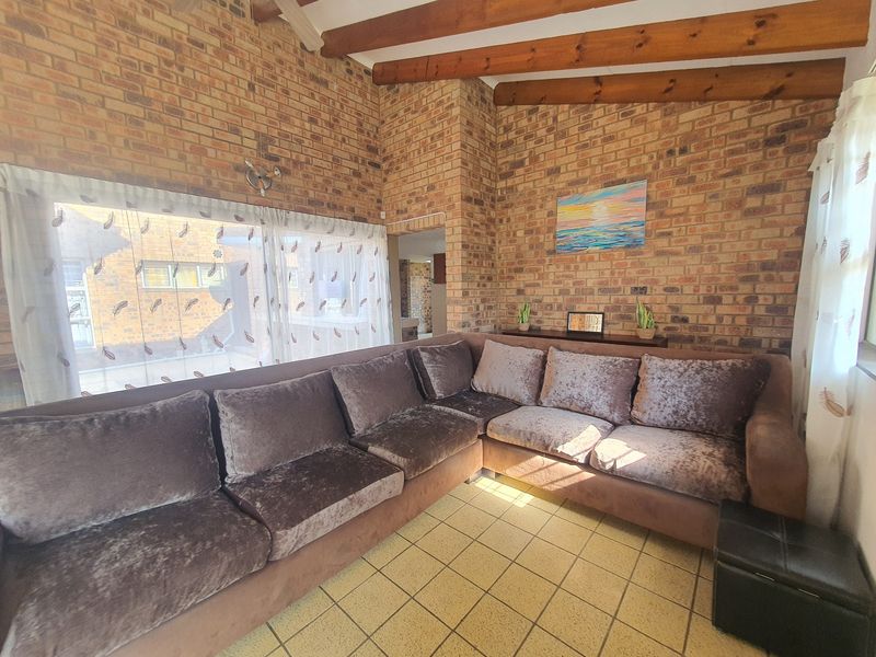 A living room featuring exposed brick walls, vaulted ceiling with timber beams, and tiled flooring, offering a rustic and character-filled living space.