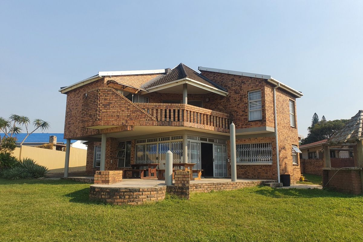 Rear view of a double-story brick house featuring a balcony, covered patio area, and a spacious lawn.