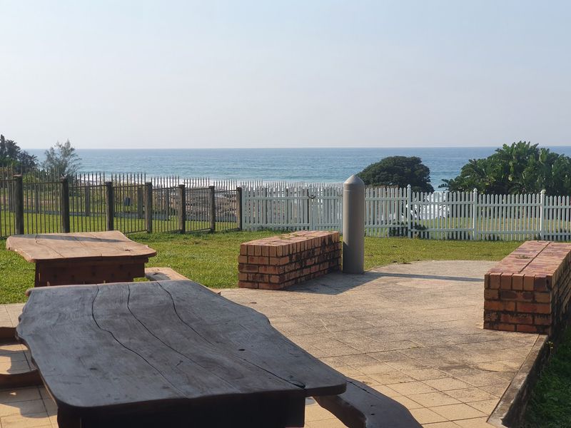 Outdoor paved patio area featuring brick seating walls and scenic ocean views, enclosed by perimeter fencing.