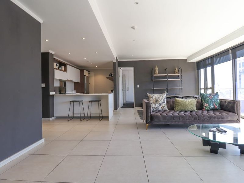 Modern open-plan living area featuring a sleek kitchen with island, tiled flooring, and expansive windows providing natural light and balcony access.