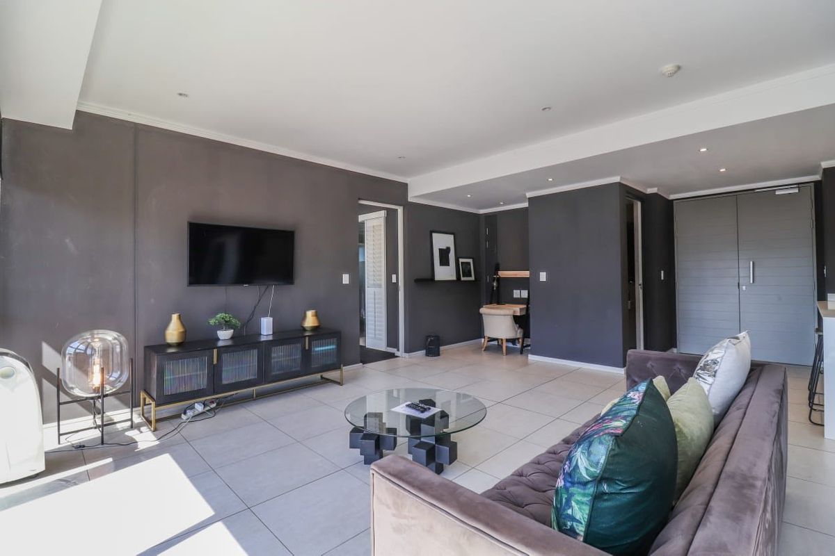 A modern, open-plan living area featuring neutral tiled flooring, recessed downlighting, and dark feature walls, creating a contemporary and well-maintained living space.