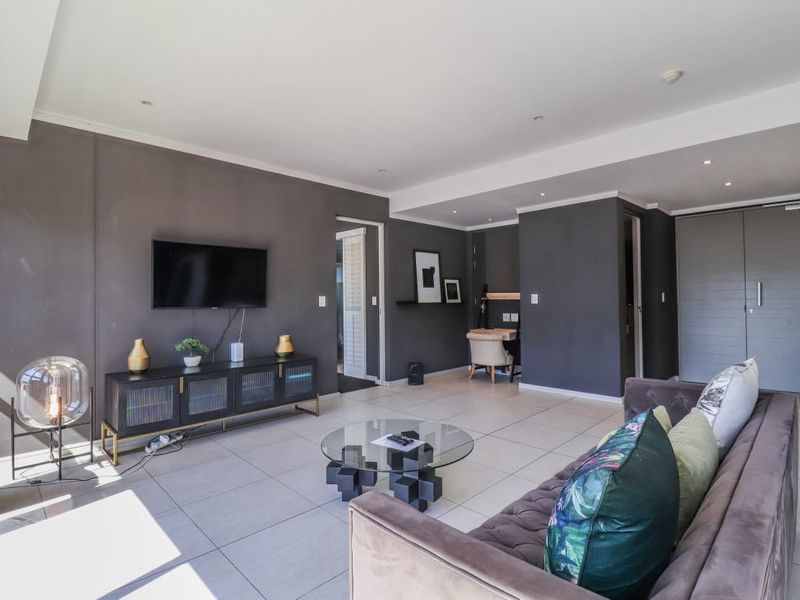 A modern, open-plan living area featuring neutral tiled flooring, recessed downlighting, and dark feature walls, creating a contemporary and well-maintained living space.