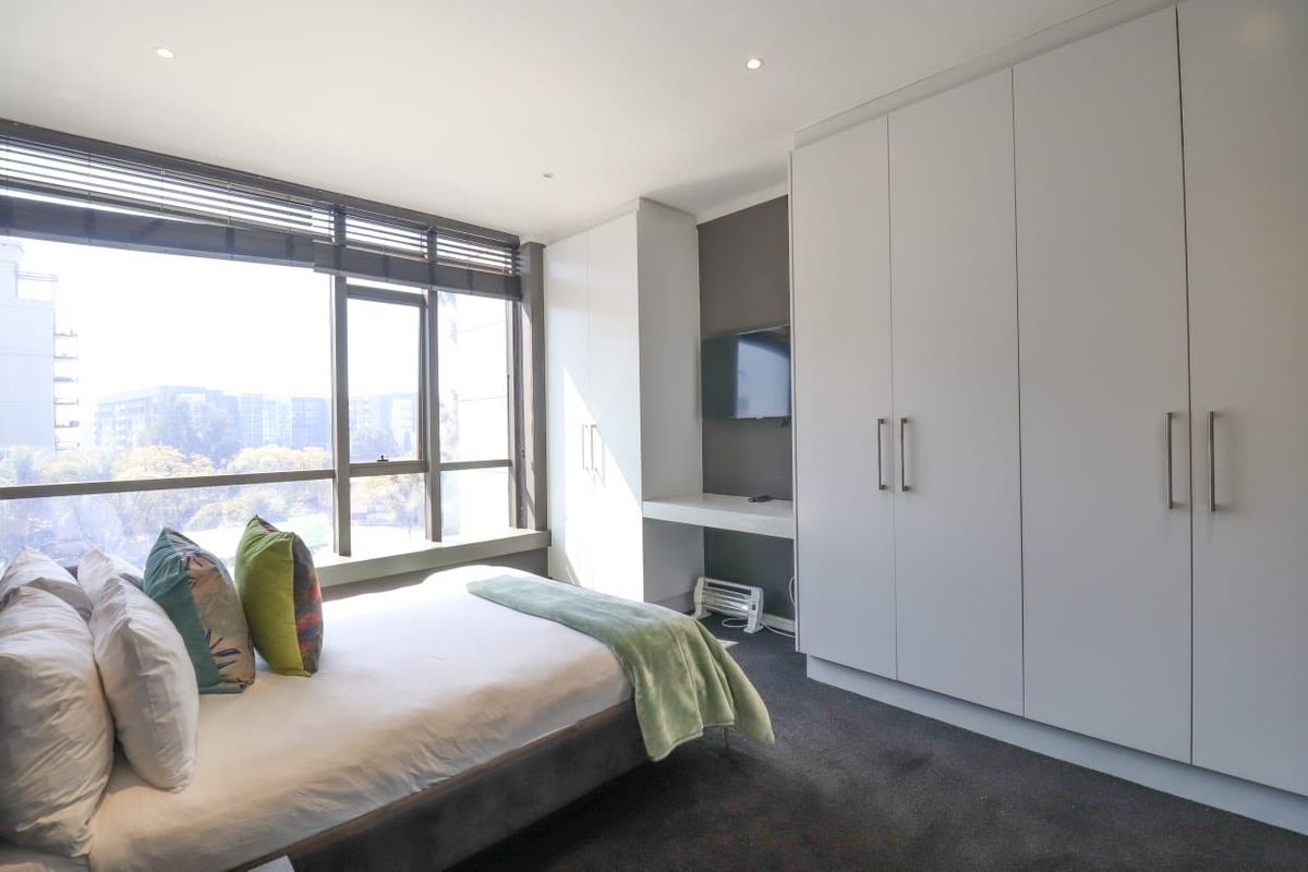 Modern bedroom featuring extensive built-in cabinetry, a dedicated desk area, and large windows providing ample natural light.