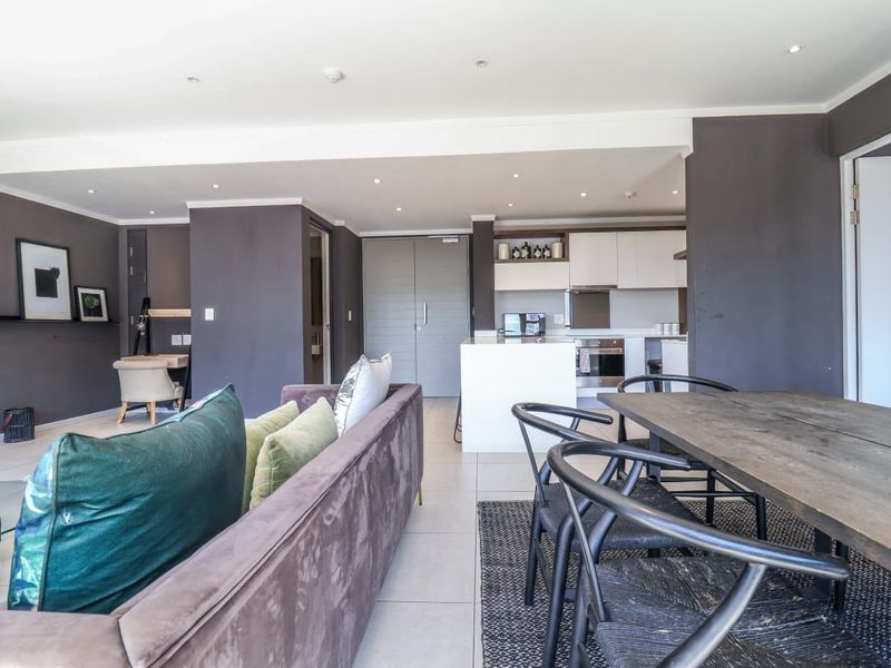 Modern open-plan living area featuring a sleek kitchen with built-in cabinetry, integrated appliances, and a central island, flowing into a spacious dining and lounge area.