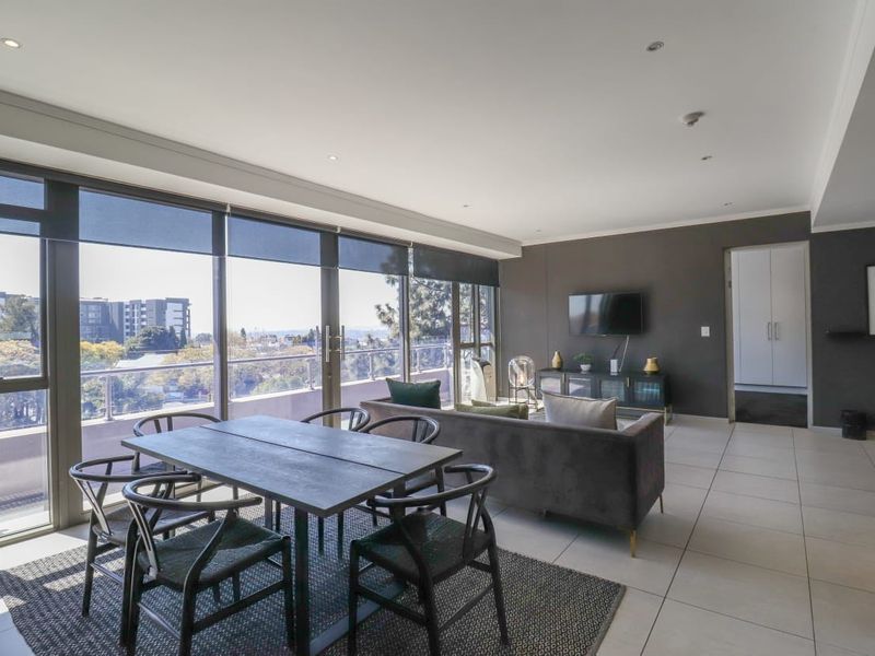 Spacious open-plan living and dining area featuring large windows with natural light, tiled flooring, and direct access to a balcony with city views.
