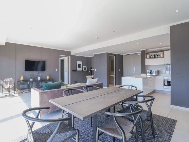 Modern open-plan living area featuring a sleek kitchen with island, integrated appliances, and spacious dining area with neutral tiled flooring throughout.