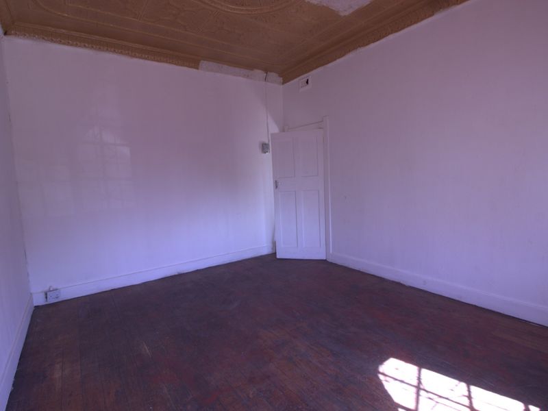 An empty bedroom featuring original timber flooring and a decorative pressed metal ceiling, offering a blank canvas for renovation.