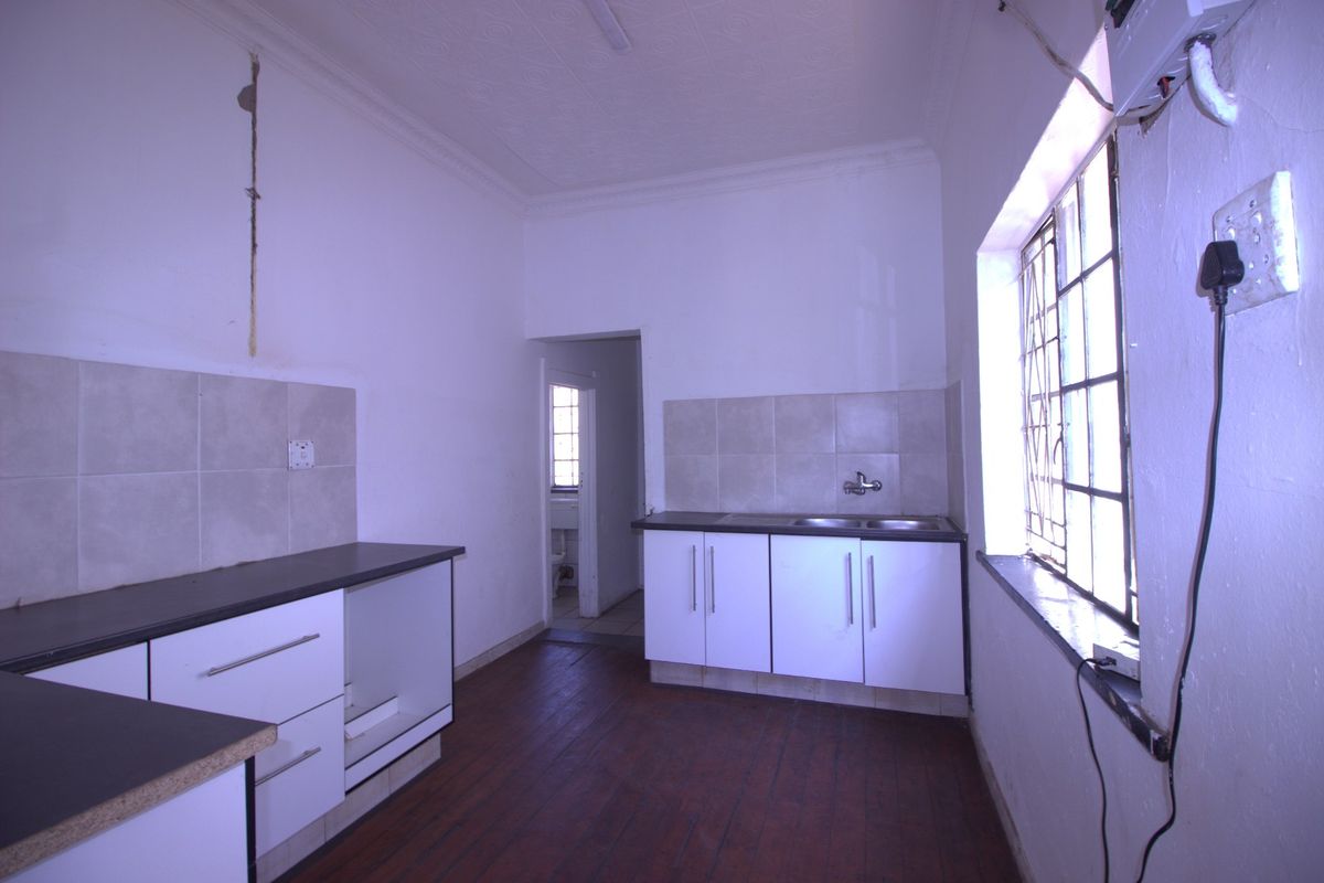 A dated kitchen featuring built-in cabinetry, laminate countertops, and a double sink, requiring cosmetic updates and repairs to wall finishes.