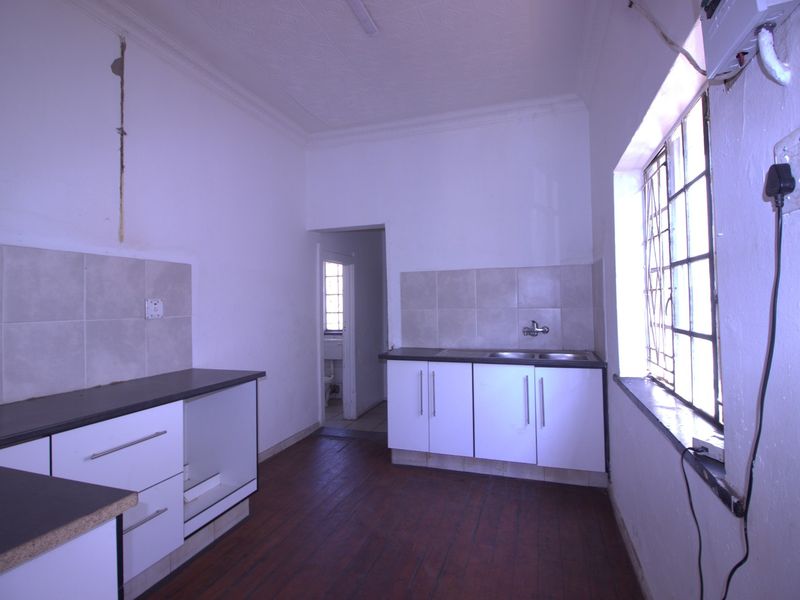 A dated kitchen featuring built-in cabinetry, laminate countertops, and a double sink, requiring cosmetic updates and repairs to wall finishes.