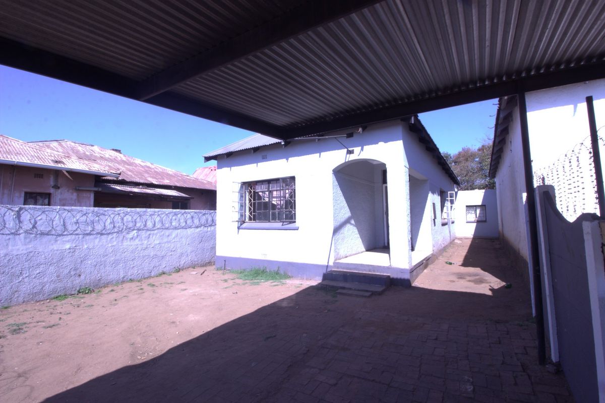Rear exterior view of the property featuring a covered carport, paved area, and secure boundary walls with razor wire.