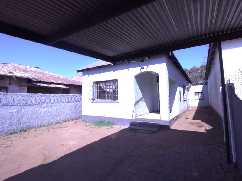 Rear exterior view of the property featuring a covered carport, paved area, and secure boundary walls with razor wire.