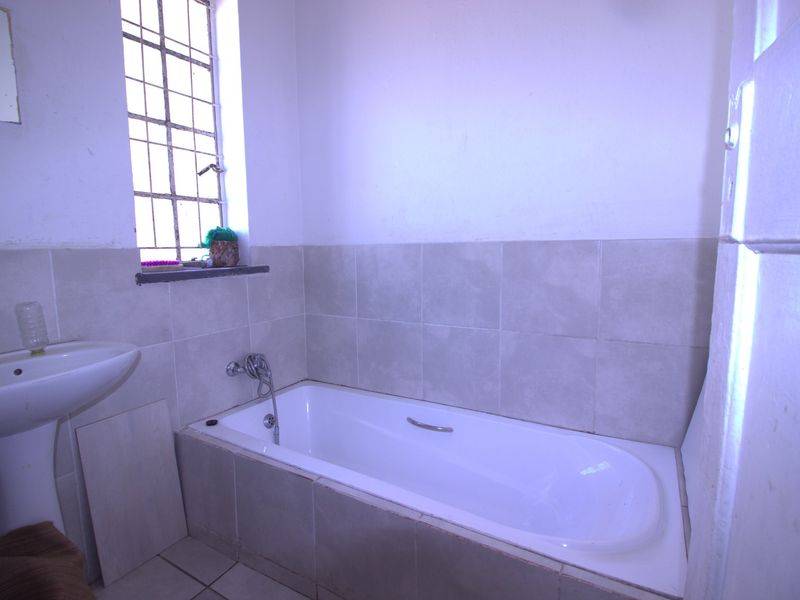 A functional bathroom featuring a pedestal basin and a built-in bathtub with tiled surround and a security window grille.