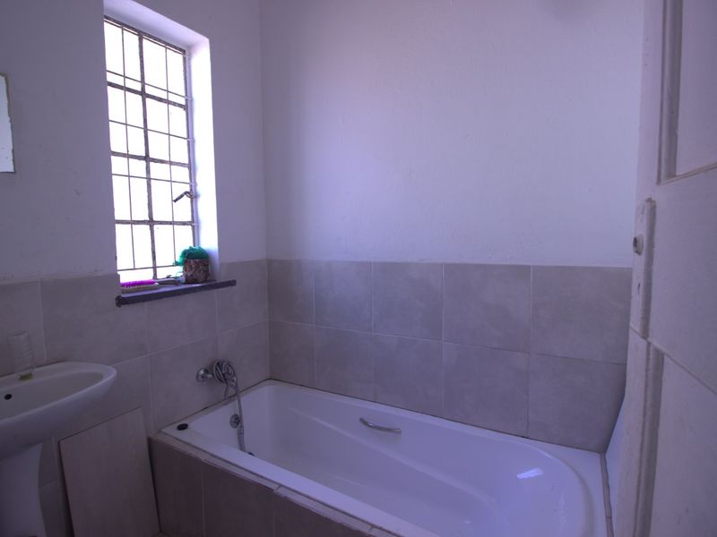 A functional bathroom featuring a pedestal basin and a built-in bathtub with tiled splashbacks and a window with security bars.