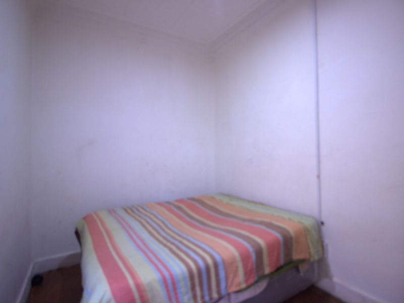 A small bedroom featuring plain white walls and timber flooring, currently requiring cosmetic updates and fresh paint to improve its overall condition.