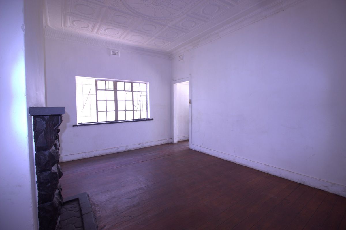 An empty living room featuring original timber flooring, a stone fireplace, and a decorative pressed metal ceiling, awaiting renovation or styling.