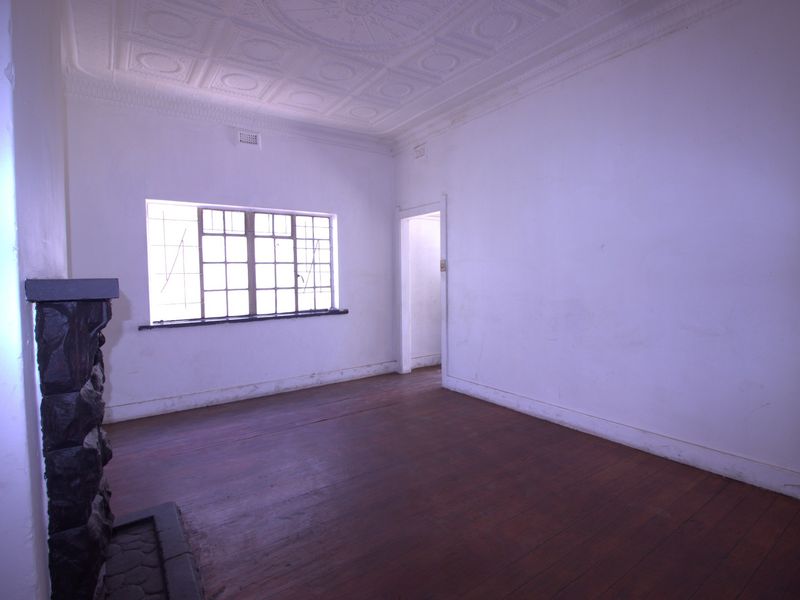 An empty living room featuring original timber flooring, a stone fireplace, and a decorative pressed metal ceiling, awaiting renovation or styling.