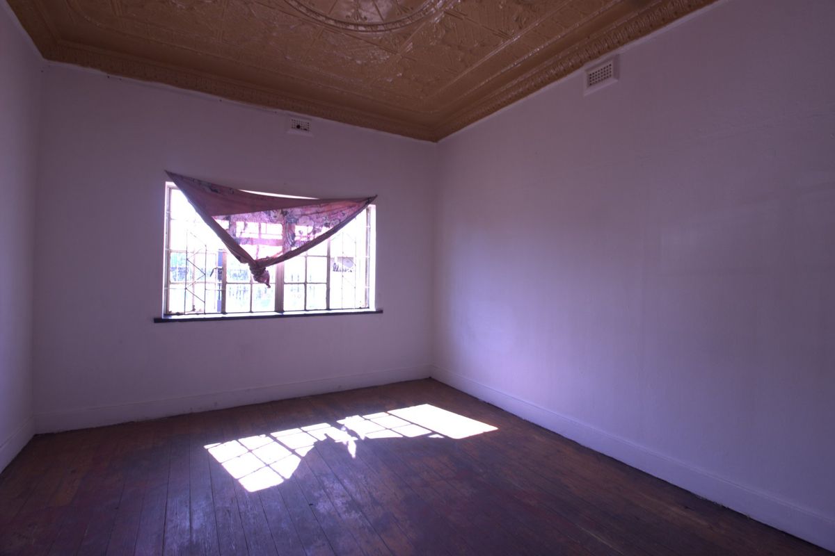 An empty bedroom featuring original pressed metal ceilings, timber flooring, and security bars on the window, offering a blank canvas for renovation.