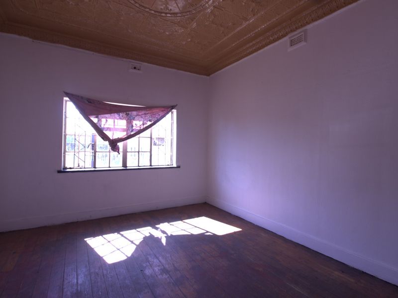 An empty bedroom featuring original pressed metal ceilings, timber flooring, and security bars on the window, offering a blank canvas for renovation.