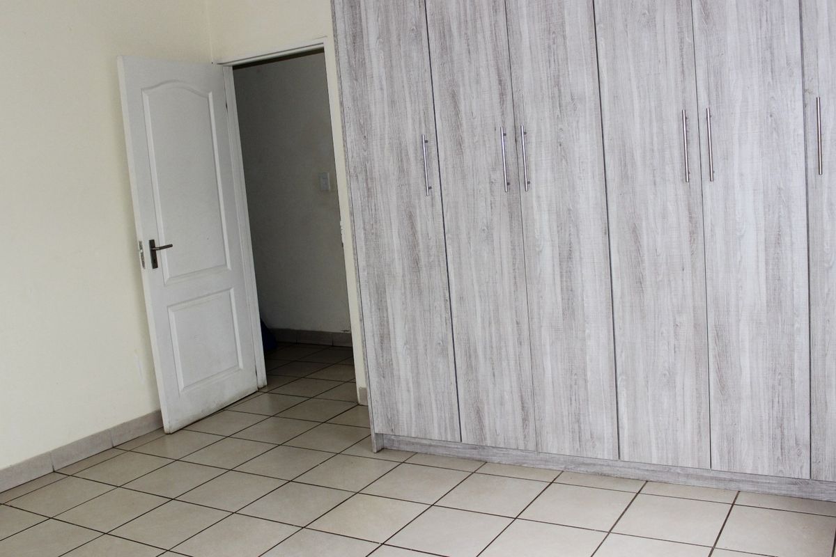 A clean, empty bedroom featuring neutral tiled flooring and modern light-wood grain built-in cupboards with silver handles.