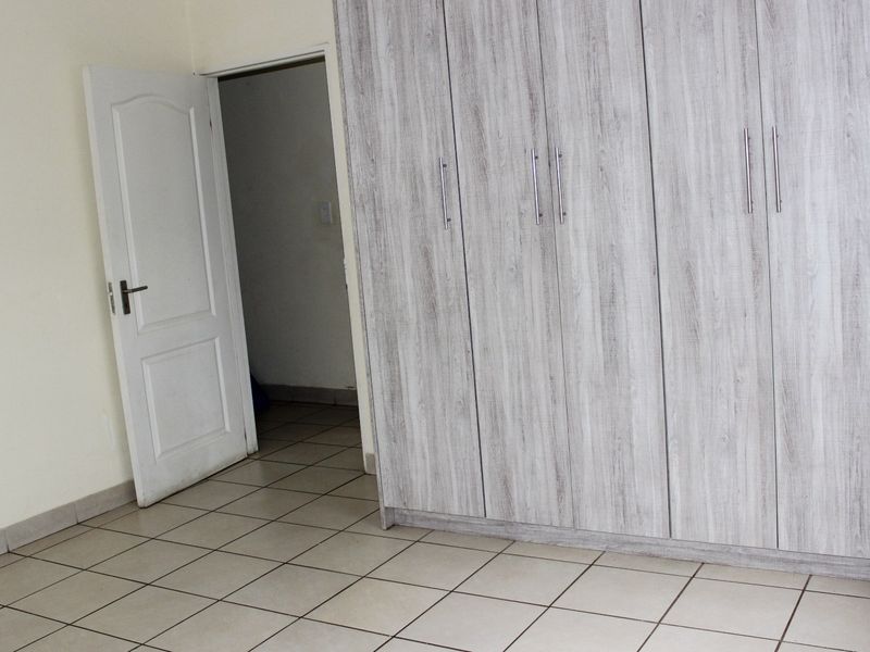 A clean, empty bedroom featuring neutral tiled flooring and modern light-wood grain built-in cupboards with silver handles.