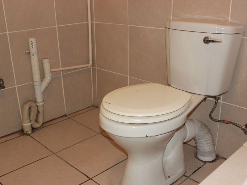A functional bathroom featuring a standard toilet with exposed plumbing and neutral ceramic wall and floor tiling.