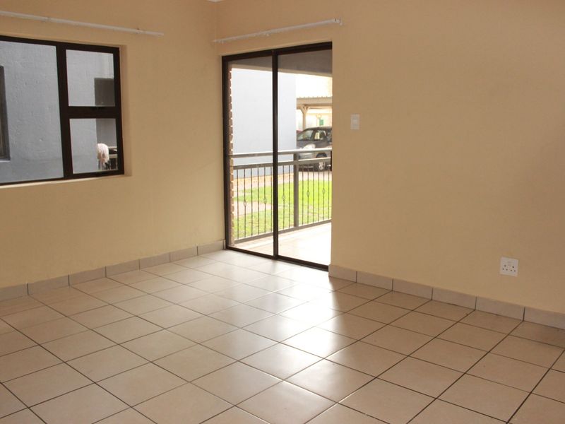 An empty living room featuring neutral tiled flooring, large sliding glass doors leading to an outdoor area, and natural light through aluminium-framed windows.
