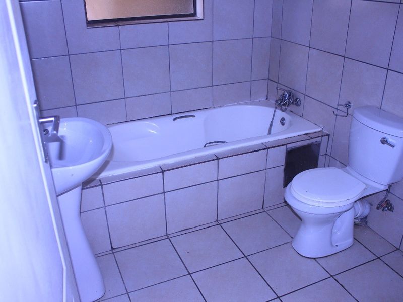 A functional bathroom featuring a pedestal basin, built-in bathtub, and toilet, finished with neutral ceramic wall and floor tiles.