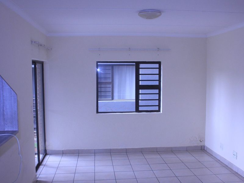An empty living room featuring tiled flooring, a sliding glass door, and a metal-framed window, providing a neutral blank canvas for interior design.