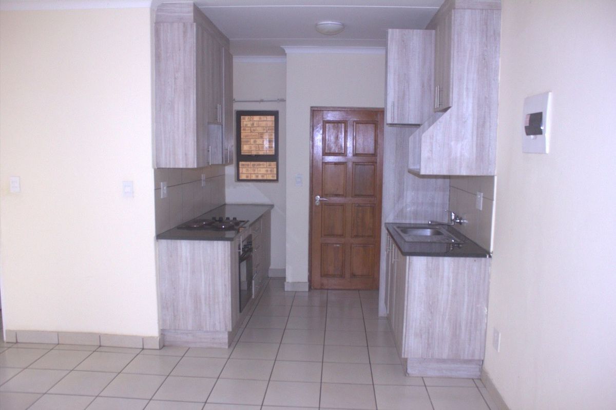 A functional galley-style kitchen featuring light wood-look cabinetry, dark countertops, built-in oven and hob, and tiled flooring.