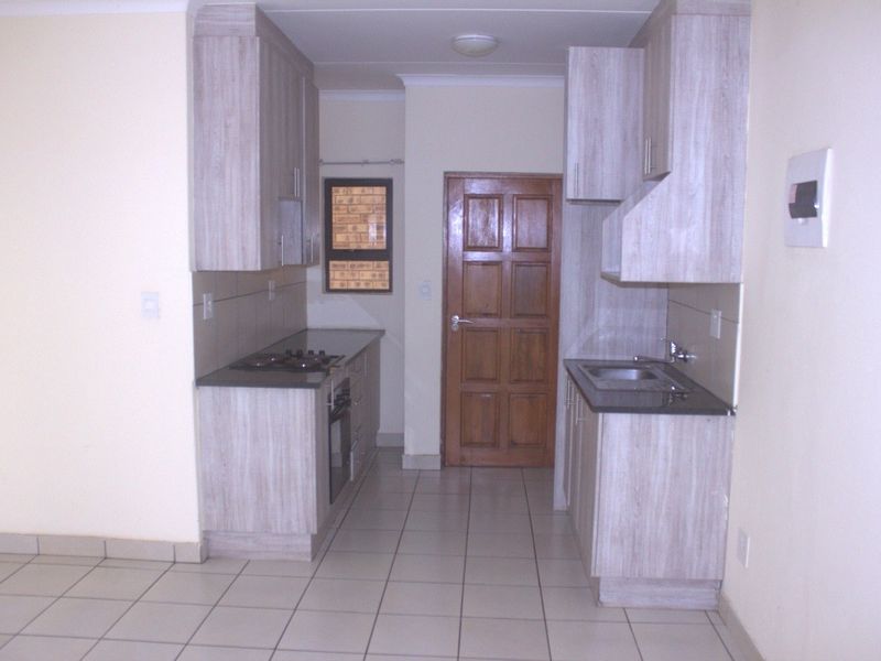 A functional galley-style kitchen featuring light wood-look cabinetry, dark countertops, built-in oven and hob, and tiled flooring.
