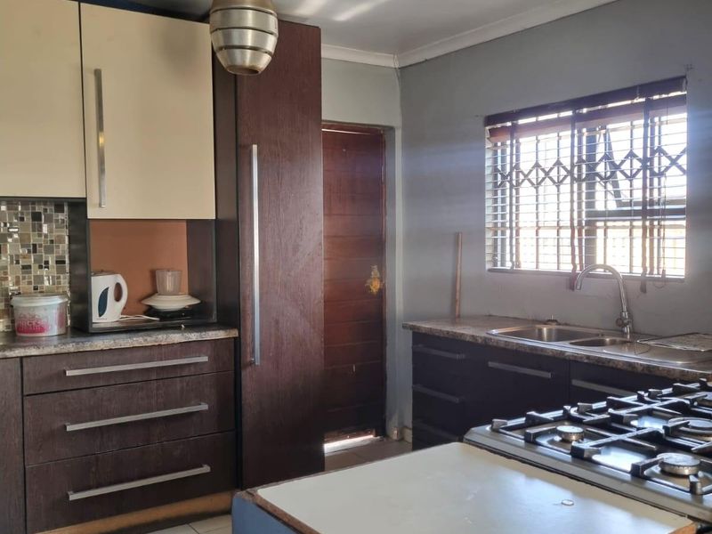 Kitchen featuring dark and cream cabinetry, a gas hob, double sink, and mosaic tile backsplash, requiring some cosmetic updates to the countertops and finishes.