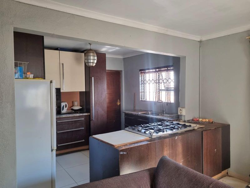 A functional kitchen featuring dark wood cabinetry, a gas hob, and a stainless steel sink, offering a practical layout with potential for modern updates.