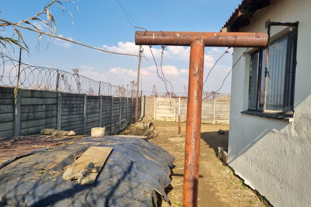 Rear exterior area featuring a precast concrete boundary wall with razor wire, a metal window frame, and an unmaintained yard space.