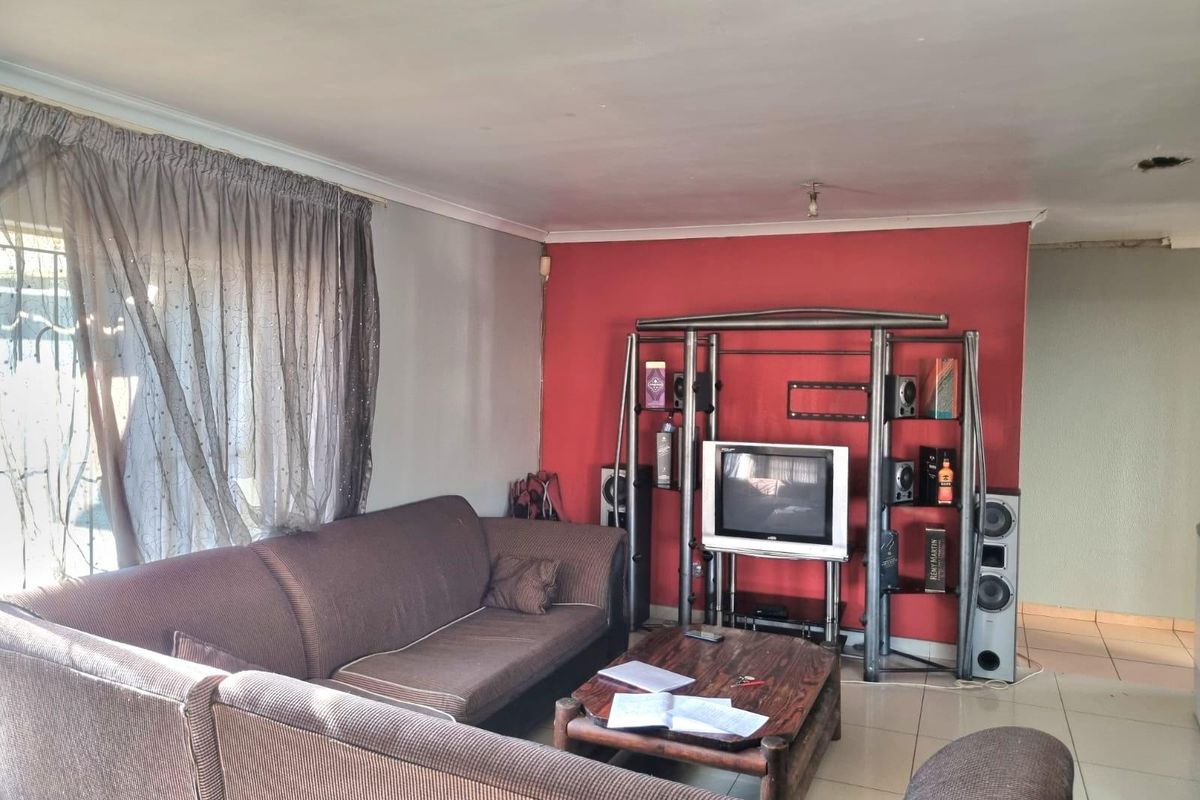 A living room featuring tiled flooring and a red accent wall, requiring minor cosmetic updates and ceiling fixture repairs.