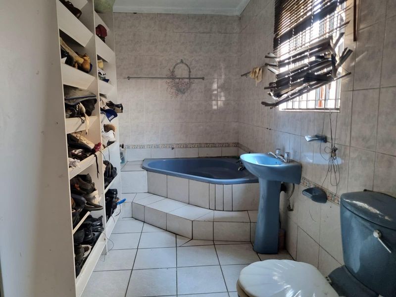 A dated bathroom featuring a corner bathtub, pedestal basin, toilet, and built-in shelving, with tiled finishes throughout.