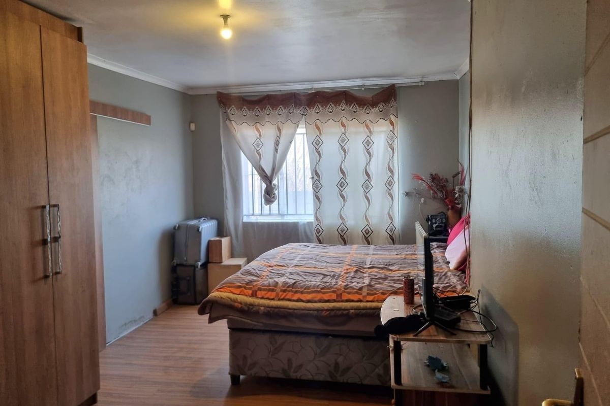 A bedroom featuring laminate flooring, a built-in wardrobe, and security bars on the window.