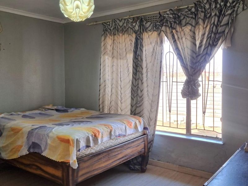 A bedroom featuring laminate flooring, security bars on the window, and a central light fixture, requiring minor cosmetic updates to the walls.