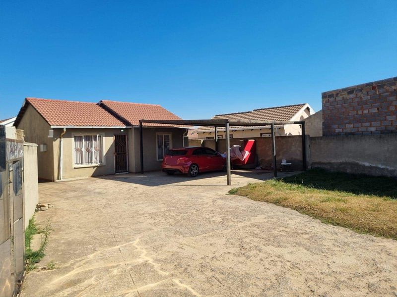 Front view of a single-story house featuring a tiled roof, a concrete driveway, and a covered carport area.