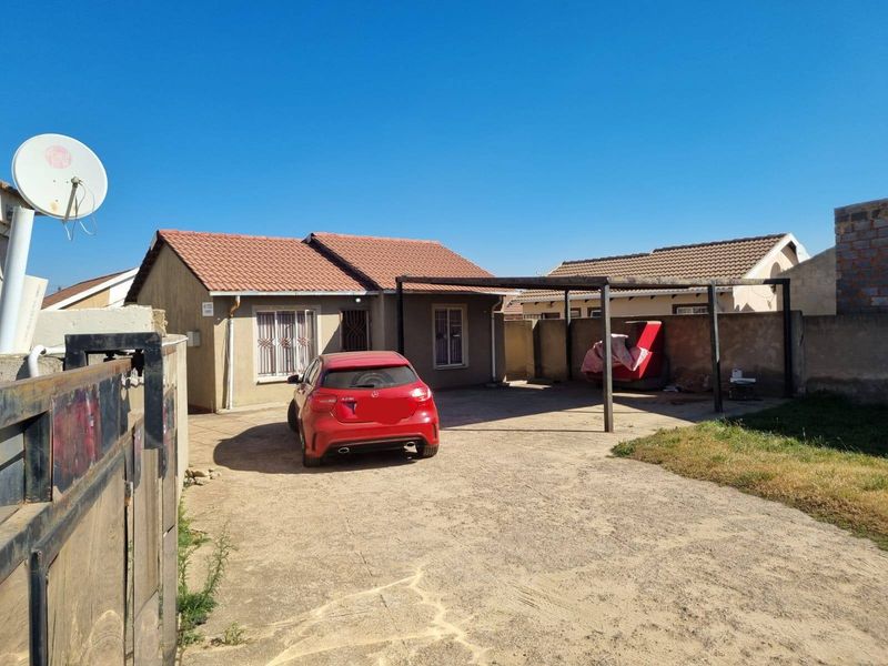 Front exterior view of a single-story house featuring a tiled roof, a carport, and a concrete driveway with boundary walling.