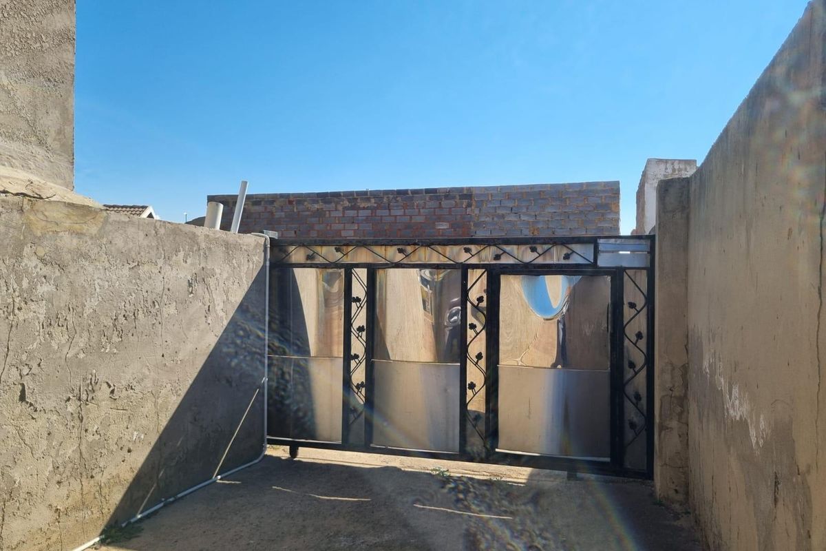 A rear exterior view featuring a metal sliding gate set between unfinished brick and concrete boundary walls.