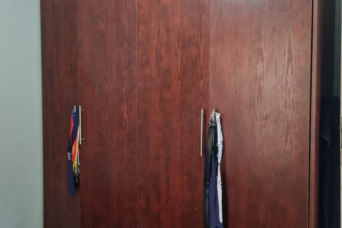 A bedroom featuring a large, dark wood-finish built-in wardrobe with modern metal handles.